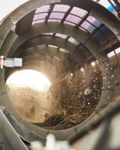 Excavator dropping untreated material into the hopper which is transferred into the barrel of the trommel to be processed