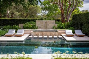 A new sandstone water feature and pool lounge area is flanked by a large eucalyptus tree, white agapanthus and clipped hedging