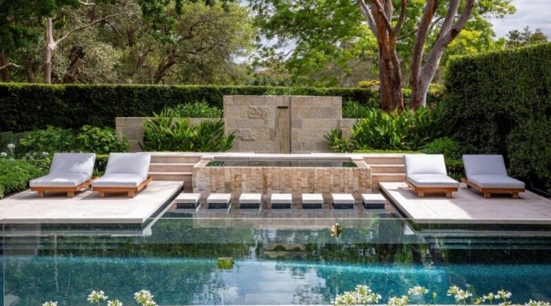 A new sandstone water feature and pool lounge area is flanked by a large eucalyptus tree, white agapanthus and clipped hedging