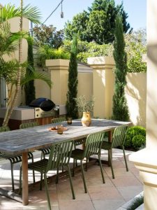 Textural planting softens the outdoor dining space, framing the timber table and built-in barbecue while bringing greenery and depth to the hardscape setting